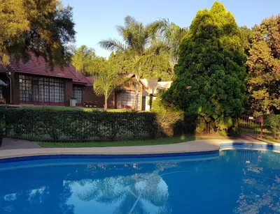 a blue swimming pool in front of a house at Falling Feather Inn in Pretoria