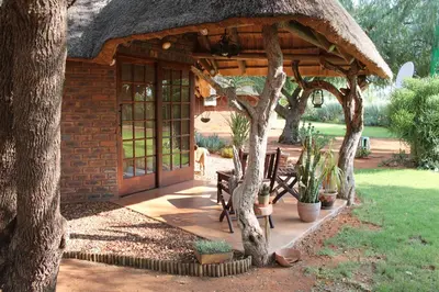 a house with a thatch roof with benches and trees at Weltevreden Country Guest Lodge in Groblersbrug