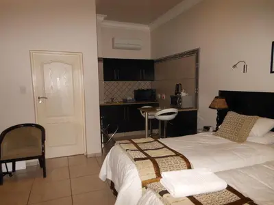 a bedroom with a large bed and a kitchen at Goodey's Guesthouse in Pretoria