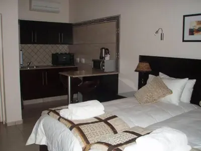 a bedroom with a bed with white sheets and a kitchen at Goodey's Guesthouse in Pretoria