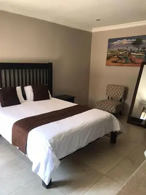a bedroom with a large bed and a chair at Kanyane Lodge in Jane Furse