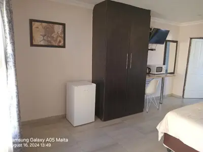 a bedroom with a brown cabinet and a desk at Kanyane Lodge in Jane Furse