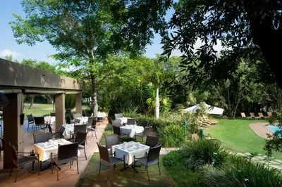 a restaurant with tables and chairs in a garden at Kruger Park Lodge in Hazyview