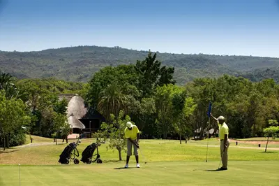 two men are playing golf on a golf course at Kruger Park Lodge in Hazyview