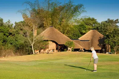 a woman is playing golf in front of some thatched at Kruger Park Lodge in Hazyview