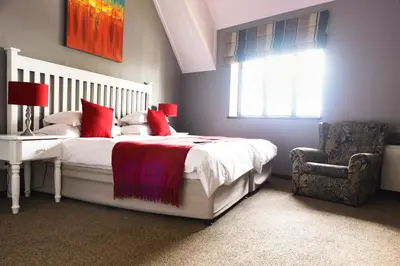 a bedroom with a bed with red pillows and a chair at Constantia Hotel and Conference Centre in Midrand