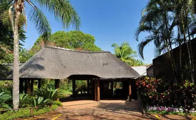 a building with a thatched roof and palm trees at Hazyview Sun in Hazyview