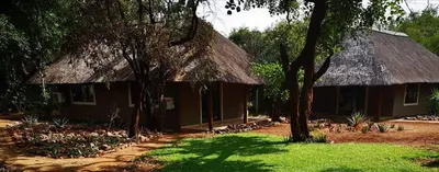 a small house with a thatched roof and a tree at Boulders Safari Lodge in Malelane