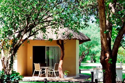 a small house with a table and chairs under a tree at Komati River Chalets in Komatipoort