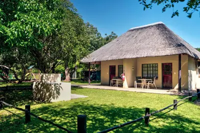 a small house with a thatched roof and a yard at Komati River Chalets in Komatipoort
