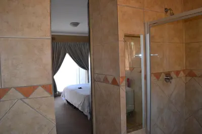 a bathroom with a shower and a bedroom with a bed at Oasis Of Life Guest House in Witbank