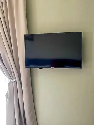 a flat screen tv hanging on a wall with a curtain at Oasis Of Life Guest House in Witbank