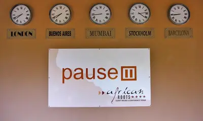 a group of clocks on a wall with a pause sign at African Roots Guest House in Polokwane