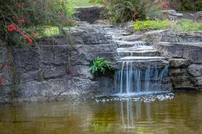 a waterfall in a pond with a stone wall at Pine Lake Resort in White River