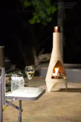 a glass of wine sitting on a table with a fireplace at Southern Sands Eco Lodge in Hoedspruit