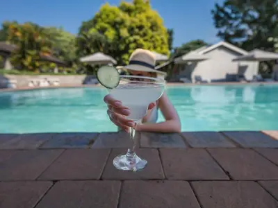 a woman holding a drink in front of a pool at ANEW Resort White River Mbombela in White River
