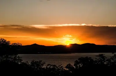 a sunset over a body of water with the sun setting at Hartbeespoortdam Lodge in Hartbeespoort