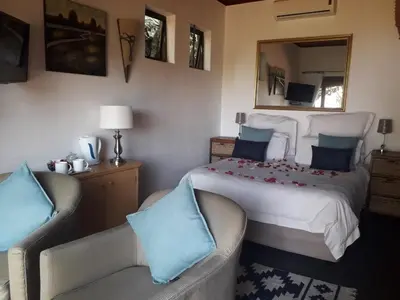 a bedroom with a large bed and two chairs at Hartbeespoortdam Lodge in Hartbeespoort