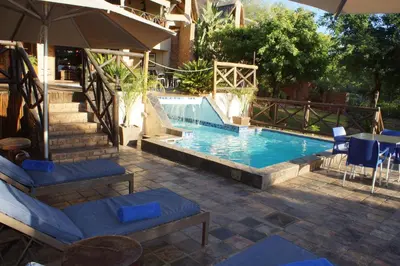 a pool with chairs and a table and an umbrella at Crocodile Kruger Safari Lodge in Marloth Park