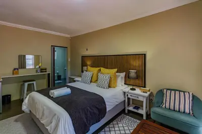 a bedroom with a large bed and a chair at Pumleni Guesthouse in Hartbeespoort