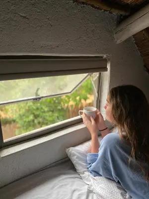 a woman holding a cup of coffee looking out a window at @Nature Luxury Cottages in Nelspruit