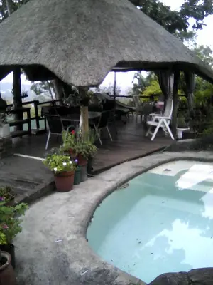 a swimming pool with a thatched umbrella and tables and chairs at Pumba's Lookout in Barberton