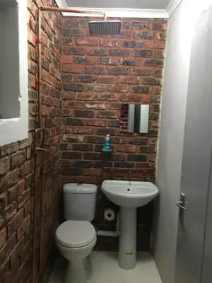 a brick walled bathroom with a toilet and a sink at Inyameko BnB in Centurion