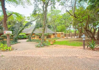 a park with a brick walkway with trees and a building at Kruger Adventure Lodge in Hazyview