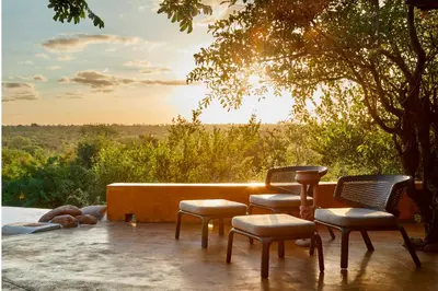 a group of chairs sitting on a patio with the sunset at Geiger's Camp in Timbavati Game Reserve by NEWMARK in Timbavati Game Reserve
