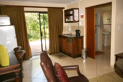 a living room with a couch and chairs and a kitchen at Selati 103 Guest Cottages in Malelane
