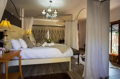 a bedroom with a large white bed with a chandelier at Tamboti Lodge Guest House in Tzaneen