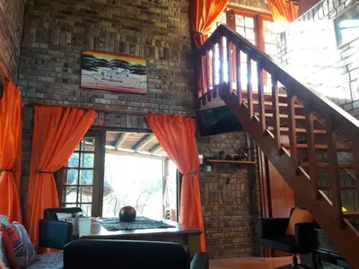 a living room with a staircase and orange curtains at Little Bush Baby in Marloth Park