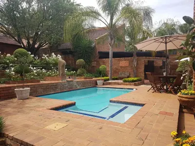 a swimming pool in a yard with a table and an umbrella at Chateau Vue Guesthouse in Pretoria