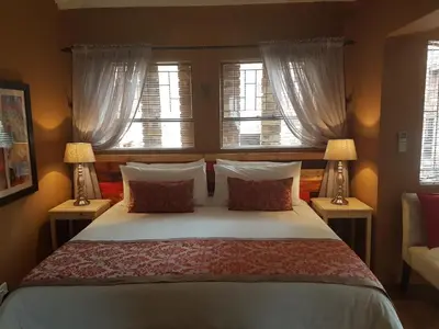 a bedroom with a bed with two lamps and two windows at Chateau Vue Guesthouse in Pretoria