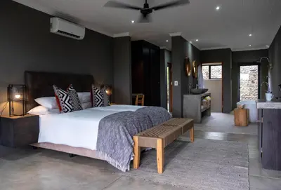 a bedroom with a large bed with a bench in it at Tamboti River Lodge in Hectorspruit