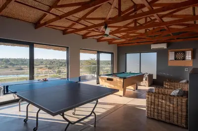 a living room with a ping pong table and windows at Tamboti River Lodge in Hectorspruit