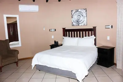 a bedroom with a white bed and a chair at Vahlavi Lodge in Giyani