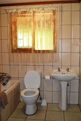 a bathroom with a toilet and a sink and a window at Log Cabin & Settlers Village in Graskop