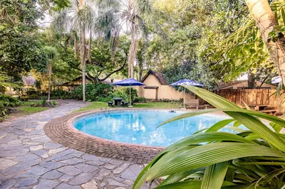 a swimming pool in a yard with umbrellas at Hotel Numbi & Garden Suites in Hazyview