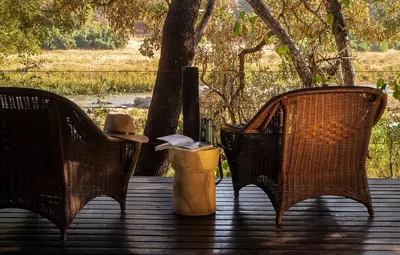 three wicker chairs and a hat sitting on a deck at Pondoro Game Lodge in Balule Game Reserve