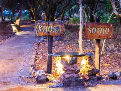 a sign that says kitzos sojo next to a fire at aha Lesedi African Lodge & Cultural Village in Pelindaba