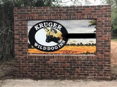 a sign on a brick wall with aiger wild dog at Kruger Wild Dog Inn in Marloth Park