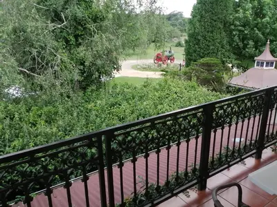 a balcony with a view of a garden and a red carriage at Silver Mist Guest House, Country Inn and Herberg in Kaapsehoop