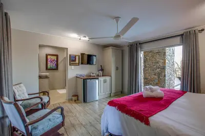 a bedroom with a bed and a chair and a window at Migdash Guesthouse in Hartbeespoort