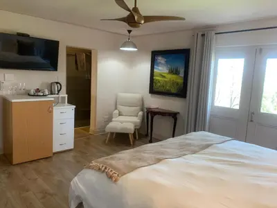 a bedroom with a bed and a chair and a ceiling fan at Migdash Guesthouse in Hartbeespoort
