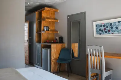 a room with a bed and a chair and a kitchen at The Wild Peach - Menlyn in Pretoria