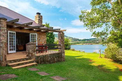 a stone cottage with a deck and a lake at Walkersons Hotel & Spa in Dullstroom