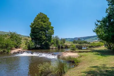 a river with a bridge and trees in the background at Walkersons Hotel & Spa in Dullstroom