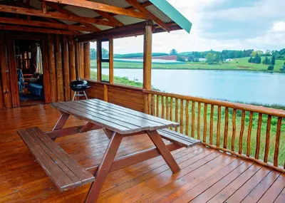 a picnic table on a deck with a view of a lake at Stanford Lake lodge in Haenertsburg