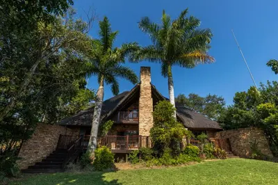 a house with a thatched roof and palm trees at Legend Safaris 257B - in Kruger Park Lodge in Hazyview